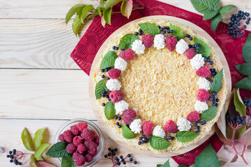 Napoleon cake with raspberries and cream on red napkin on light wooden background. Overhead view