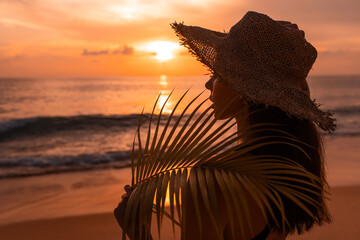 Woman with straw hat on the beach at sunset