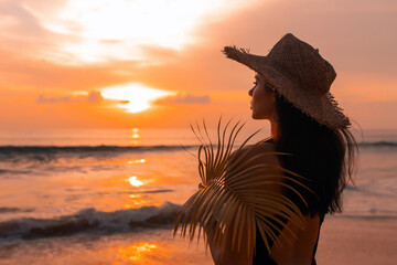 Woman with straw hat on the beach at sunset