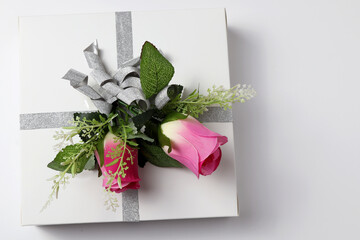 A gift box or gift wrapped in paper and a rose flower on a white table Flat styling Copy space for text