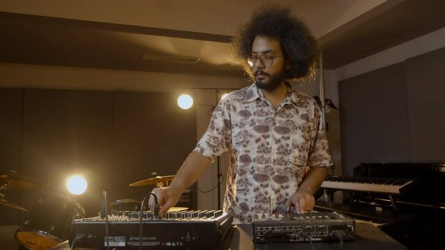 Music production studio. Beatmaking. Hispanic man recording new beats. An intelligent brunette male person with afro hair records his ideas.