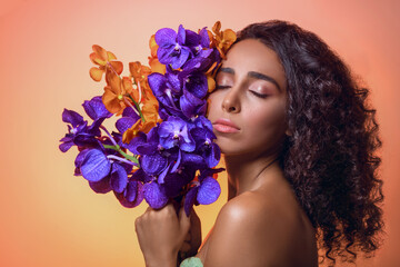 Beautiful woman with bright purple makeup. Young caucasian gorgeous adult girl with long brown curly hair. Model. Closeup woman's portrait with flowers. Vivid make-up. Sexy female.