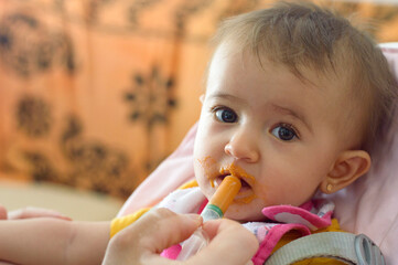 Primer plano de un bebé comiendo con jeringa mirando a la cámara