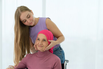 Young daughter embracing her sick mom who wearing headscarf on wheelchair, giving support battling...