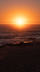 Bright orange sun on horizon over ocean. Summer afternoon on beach in Portugal. Vertical aspect ratio.