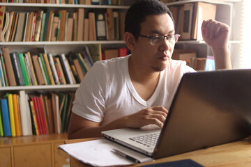 Asian muslim man studying in library, exam preparation concept. Male college student using laptop to learn online
