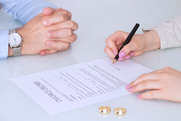 Hands of wife, husband signing decree of divorce, dissolution, canceling marriage, legal separation documents, filing divorce papers or premarital agreement prepared by lawyer. Wedding ring