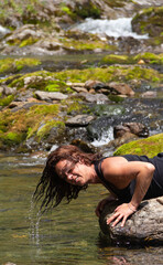 Girl wetting her hair and cooling off in a high mountain river with unfocused background. Photograph taken in the Aran valley, Lerida-Spain.