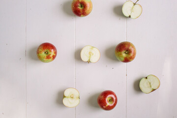Flat-lay concept of red apples on a white wooden background, view from above, half apples
