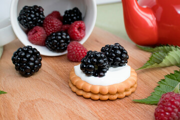 Biscuits with berries and creamy cream. A healthy dessert. selective focus. Mix of blackberries and raspberries. next to a red teapot with hot tea. concept of a useful tea party.