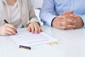 Hands of wife, husband signing decree of divorce, dissolution, canceling marriage, legal separation documents, filing divorce papers or premarital agreement prepared by lawyer. Wedding ring