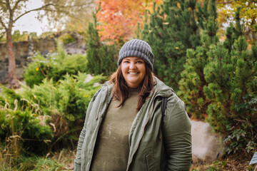 Young  cheerful curvy woman in grey hat and green jacket walking in the park