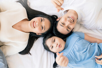 Happy Attractive Young asian Family Portrait Healthy harmony in life family day concept asian family man woman and little girl having good time together.top view bedroom mattress