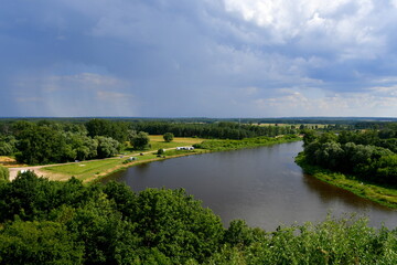 Fototapeta na wymiar A view from the top of a hill with a vast yet shallow river or lake flowing through some forests and moors with a cloudy sky right before the thunderstorm visible in the distance seen in Poland
