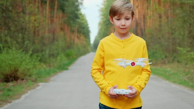  Boy lift off the drone using remote control. Child launches the drone outdoors. Boy plays with a quadrocopter on the nature. White boy is learning  to control a drone in the Park. Slow motion  video