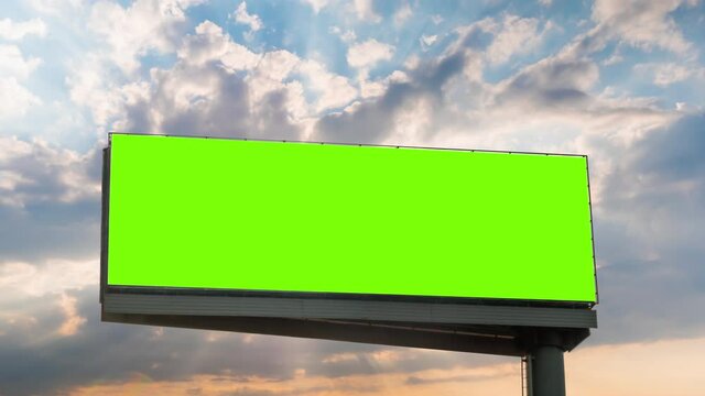 Timelapse: blank wide green billboard or large display with sun beams shining through clouds at sunset. Consumerism, time lapse, advertising, green screen, mock up, copy space, chroma key concept