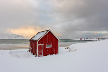 Lofoten Islands in Norway and their beautiful winter scenery at sunset. Idyllic landscape with red house on snow covered beach. Tourist attraction in the arctic circle.