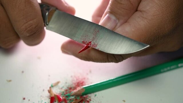 Footage of hands slowly sharpening a pencil and some coloured pencils with a sharp knife.