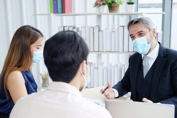 Caucasian Senior manager meeting with asian teamwork and businesspeople wearing mask preventing for Covid 19 virus. New normal and Social distancing in Office Concept.