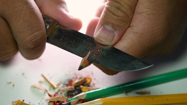 Footage of hands slowly sharpening a pencil and some coloured pencils with a sharp knife.