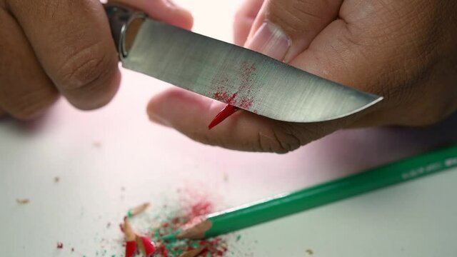 Footage of hands slowly sharpening a pencil and some coloured pencils with a sharp knife.
