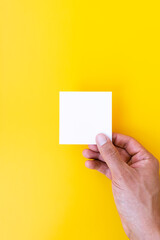 Hand with a blank sheet of paper on a yellow background. Horizontal photo.