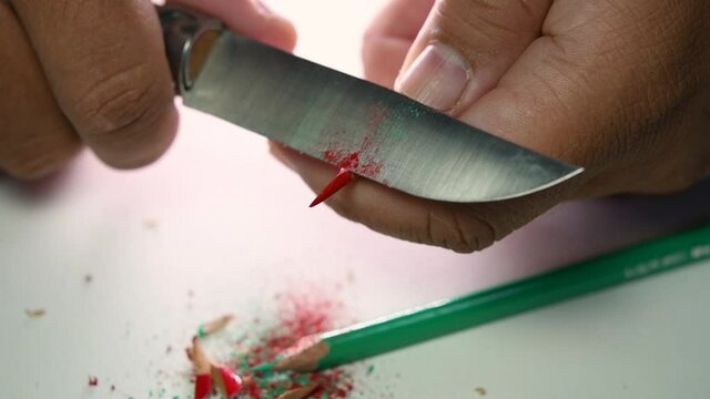 Footage of hands slowly sharpening a pencil and some coloured pencils with a sharp knife.