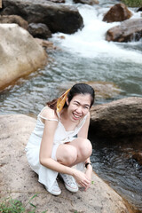 Smiling Asian woman sitting on the rocky in natural and stream in forest.
