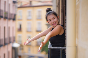young happy and beautiful Asian Korean woman in hair bun enjoying city view from hotel room balcony in Spain during holidays trip in Europe smiling cheerful in urban background
