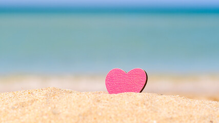 Pink heart on a sandy beach against the background of the sea. Vacation concept by the sea
