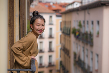 Fototapeta na wymiar young happy and beautiful Asian Chinese woman in hair bun enjoying city view from hotel room balcony in Spain during holidays trip in Europe smiling cheerful