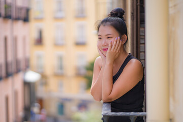 young happy and beautiful Asian Chinese woman in hair bun enjoying city view from hotel room balcony in Spain during holidays trip in Europe smiling cheerful