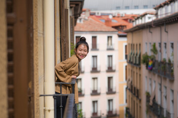 Obraz na płótnie Canvas young happy and beautiful Asian Japanese woman in hair bun enjoying city view from hotel room balcony in Spain during holidays trip in Europe smiling cheerful