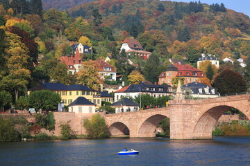 Obraz premium Scenic view of Heidelberg Old Bridge over the river Neckar with houses on the hill during sunset in autumn in Heidelberg, Germany