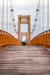 An orange steel structure suspension bridge with wooden plank floor in public park. Selective focus at wooden floor's part.