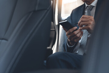 Businessman sitting on backseat in a car messaging on mobile phone digital notepad with electronic pen