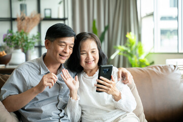 Social distancing or new normal concept.Senior asian couple sitting on sofa in home playing...