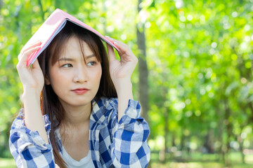 Beautiful Asian woman relaxes in the park and puts a book on her head. Happy holiday life concept