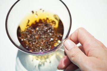 Female hand touch transparent cup with black flower tea. Incredibly beautiful shining bokeh in the water. Top view.