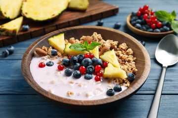 Tasty granola with yogurt, berries and sliced pineapple served for breakfast on blue wooden table