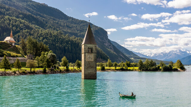 Fisherman in his boat near the submerged bell tower in Resia lake, Curon, South Tyrol, Italy