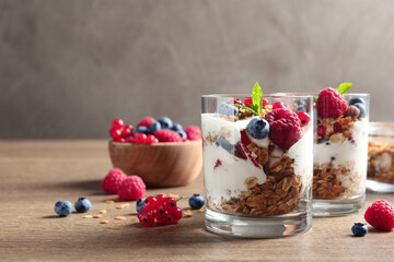 Tasty dessert with yogurt, berries and granola on wooden table, space for text