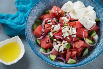 Close-up of salad with watermelon cubes, feta cheese, cucumber, red onion and balsamic sauce in a blue plate, studio shot