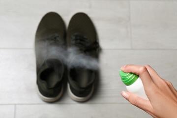 Woman spraying deodorant over pair of shoes at home, closeup