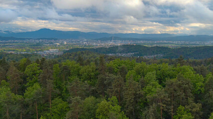 Fototapeta na wymiar AERIAL: Golden sunbeams shine through grey clouds and onto the city of Ljubljana