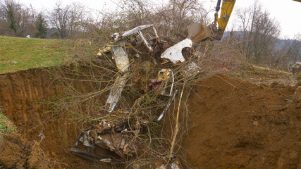 CLOSE UP: Rusty car parts and wild shrubbery gets buried in the brown soil.