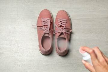 Woman spraying deodorant over pair of shoes at home, closeup - Powered by Adobe