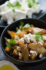 Fototapeta na wymiar Closeup of a black bowl with baked potato wedges served with feta cheese in a greek style, vertical shot, selective focus