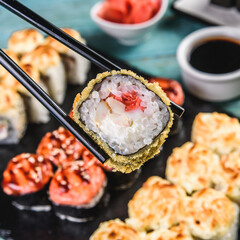 close up of chopsticks taking portion of sushi roll on the table restaurant
