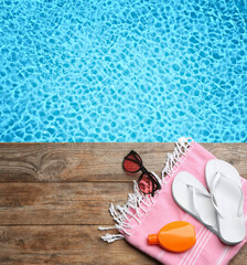 Beach accessories on wooden deck near swimming pool, flat lay. Space for text